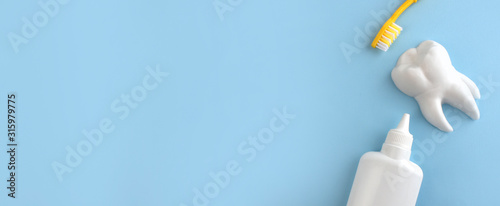 Flat lay composition with oral care products. Tooth model, teethbrush and bottle of tongue cleaner on blue background. Teeth hygiene and dental care concept. Banner with copyspace.