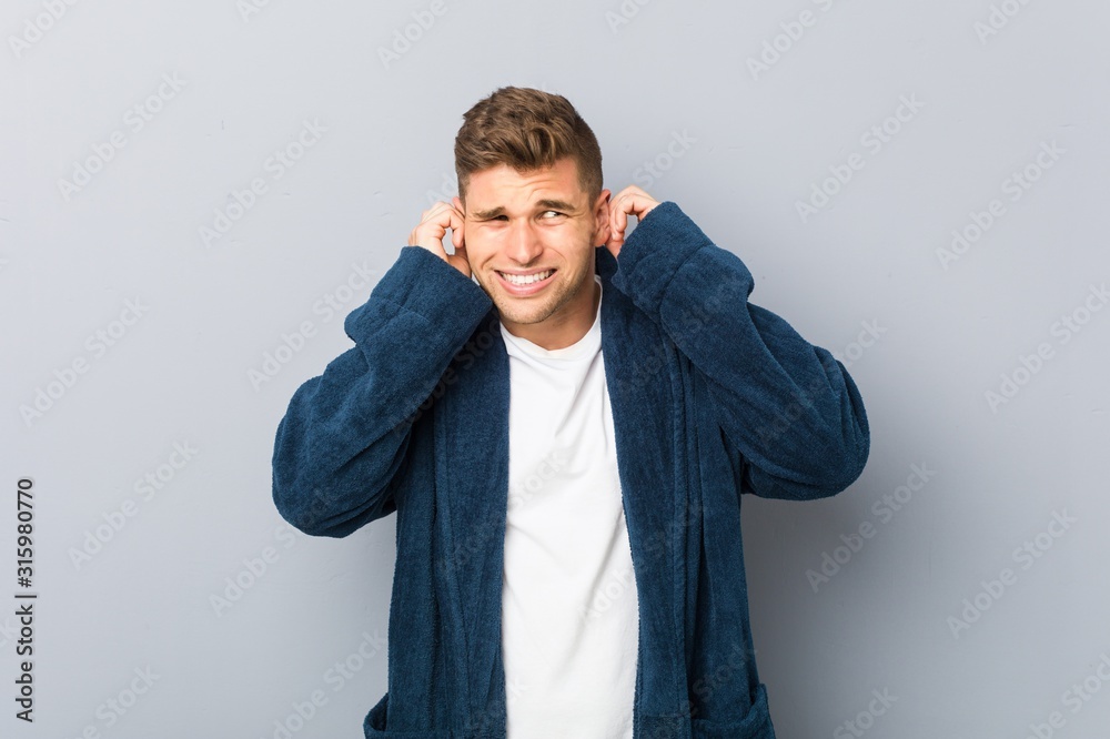 Young caucasian man wearing pajama covering ears with hands. Young caucasian man wearing pajama covering ears with hands.