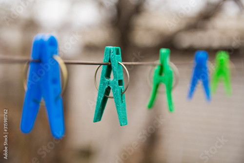 Multicolored clothespins hang on a wire in the courtyard of a village house. Autumn. The concept of the old-fashioned way of life. Drying clothes after washing. Selective focus on the turquoise one