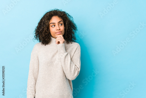 Young african american curly hair woman looking sideways with doubtful and skeptical expression.