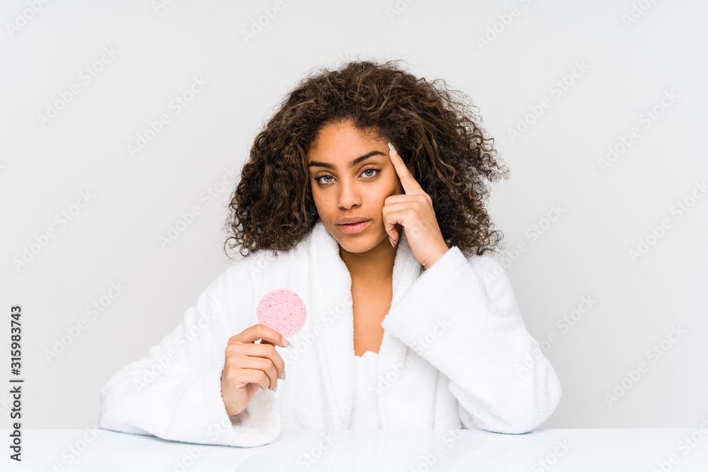 Young african american woman using a facial disk pointing his temple with finger, thinking, focused on a task. Young african american woman using a facial disk pointing his temple with finger, thinking, focused on a task.