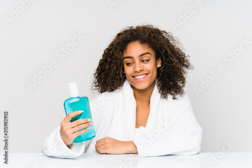 Young african american woman holding a mouth wash smiling confident with crossed arms.