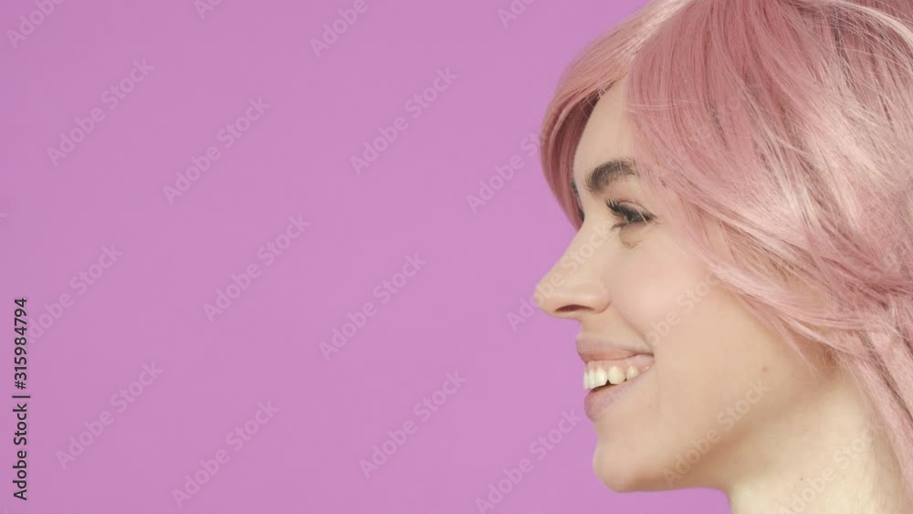 Slow-motion profile close-up of adorable young woman in kawaii pink wig, laughing and smiling, watching with excitement interesting, funny performance, standing purple background joyful Slow-motion profile close-up of adorable young woman in kawaii pink wig, laughing and smiling, watching with excitement interesting, funny performance, standing purple background joyful