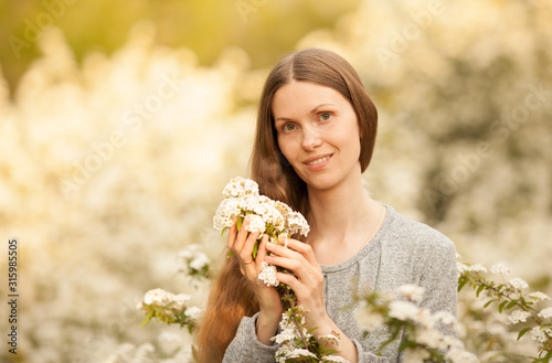 A beautiful European girl in the spring in a blooming garden, holding flowers in her hands, looking at the camera and smiling. Place for the inscription. Concept: spring. March 8. Natural beauty.