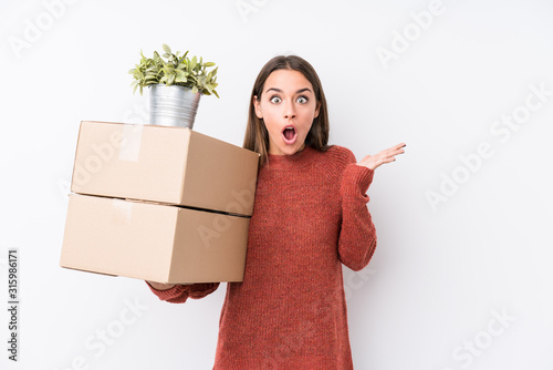 Young caucasic woman holding boxes isolated surprised and shocked.