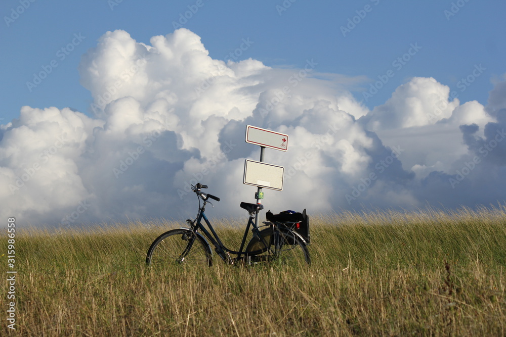 a bicycle against a sign post at the sea dyke along the westerschelde and big white clouds in a blue sky