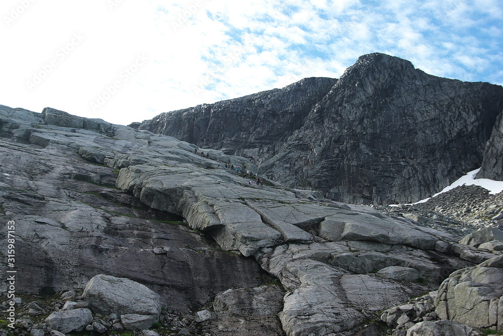 Group of hikers climbing on the impressive granite slope to Tvillingene peak in the mountain range of Seven Sisters in Helgeland on sunny summer day Group of hikers climbing on the impressive granite slope to Tvillingene peak in the mountain range of Seven Sisters in Helgeland on sunny summer day
