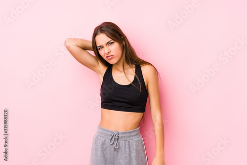 Young caucasian fitness woman posing in a pink background suffering neck pain due to sedentary lifestyle.