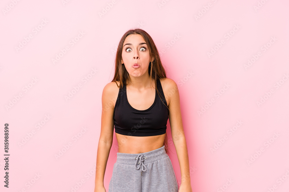 Young caucasian fitness woman posing in a pink background shrugs shoulders and open eyes confused. Young caucasian fitness woman posing in a pink background shrugs shoulders and open eyes confused.