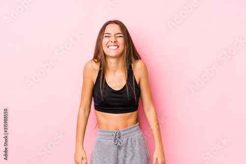 Young caucasian fitness woman posing in a pink background laughs and closes eyes, feels relaxed and happy. © Asier