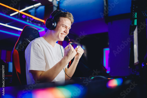 Streamer young man rejoices in victory professional gamer playing online games computer with headphones, neon color photo