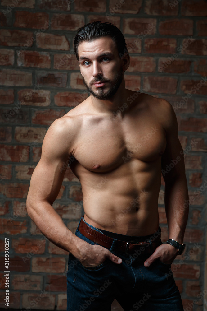 Young attractive athletic guy with a naked torso on a background of a brick wall.
