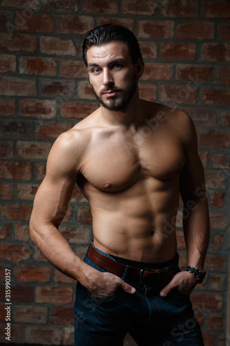 Young attractive athletic guy with a naked torso on a background of a brick wall.