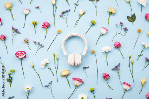 Scattered fresh colorful flowers on blue table with a n earphones in the centre