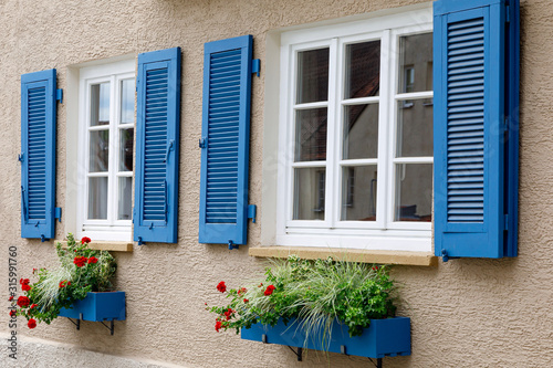 Two windows with white wooden frames  blue shutters and decorative flower boxes. Image of trendy decor  comfort  beautification.