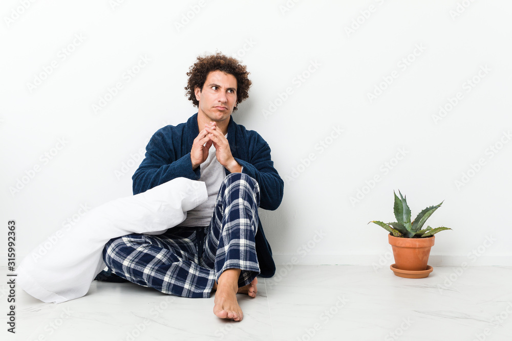 Mature man wearing pajama sitting on house floor making up plan in mind, setting up an idea. Mature man wearing pajama sitting on house floor making up plan in mind, setting up an idea.