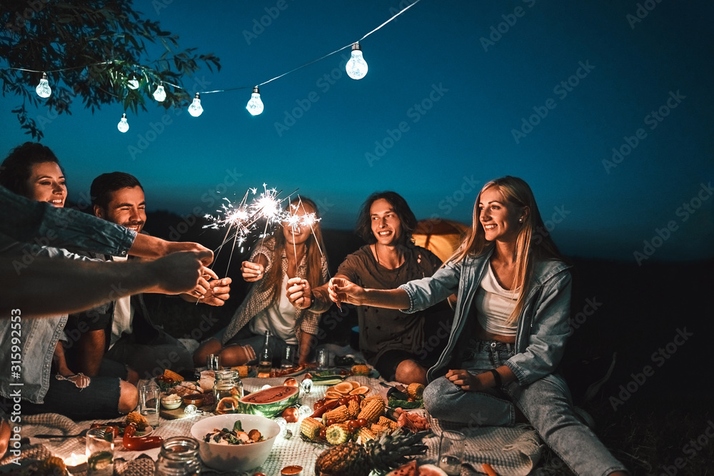 Group of friends enjoying out with sparklers. Young men and women enjoying with fireworks - obrazy, fototapety, plakaty 