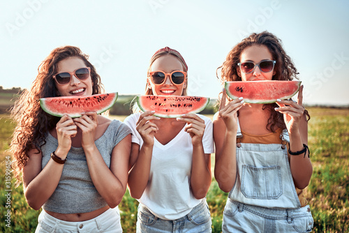 Three nice girls having fun eating watermelon In the park.