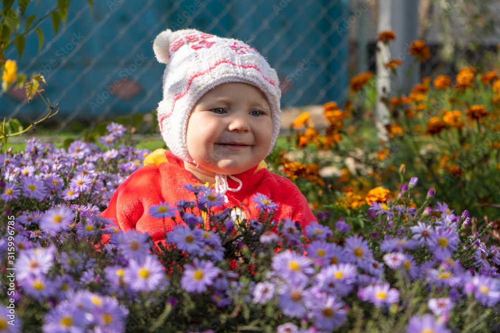 smiling baby in flowers,happy baby standing in the autumn flowers in the garden smiling baby in flowers,happy baby standing in the autumn flowers in the garden
