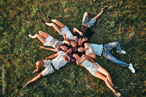 Fototapeta Group of young people having fun in park, lying on the grass