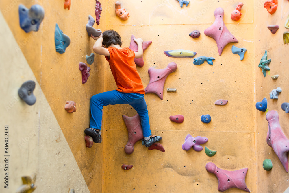 Boy climbing on artificial boulders wall in gym Boy climbing on artificial boulders wall in gym
