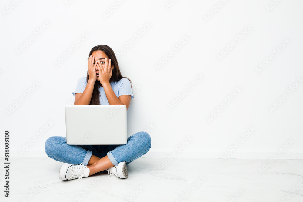Young mixed race indian woman sitting working on laptop blink through fingers frightened and nervous. Young mixed race indian woman sitting working on laptop blink through fingers frightened and nervous.