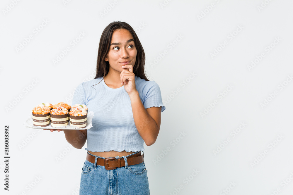 Young mixed race indian holding a sweet cakes looking sideways with doubtful and skeptical expression. Young mixed race indian holding a sweet cakes looking sideways with doubtful and skeptical expression.