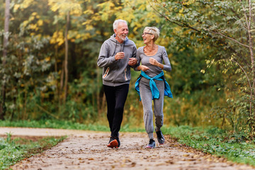 Cheerful active senior couple jogging in the park. Exercise together to stop aging.