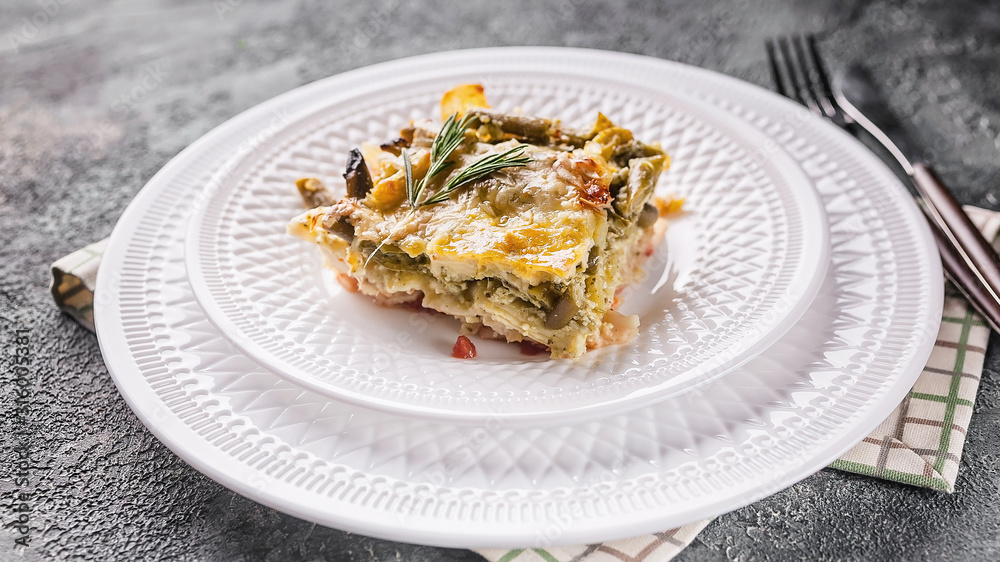 Close up baked vegetable lasagna with green beans and cheese on a white plate. Delicious vegetarian food.
