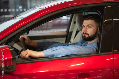 Attractive bearded man sitting in a new automobile at the dealership. Driving, buying car concept