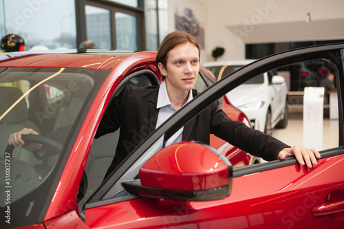 Young man choosing new car to buy at the dealership. Businessman buying new auto, getting into the vehicle