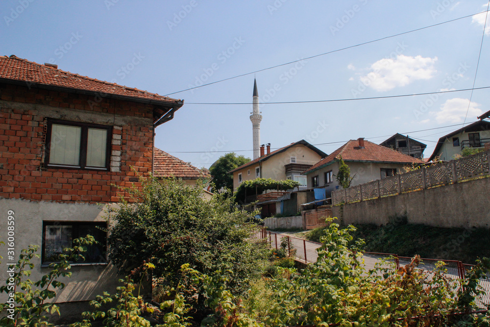 cozy rural houses among the trees and the river with visible minarets of the mosque. Architecture of residential buildings in Bosnia and Herzegovina.