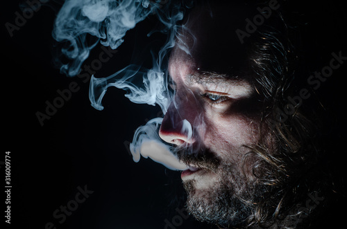 Side profile of a smoking man in low key exhaling, islolated, with copy space.