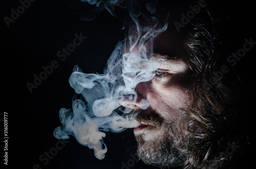 Side profile of a smoking man in low key exhaling, islolated, with copy space.