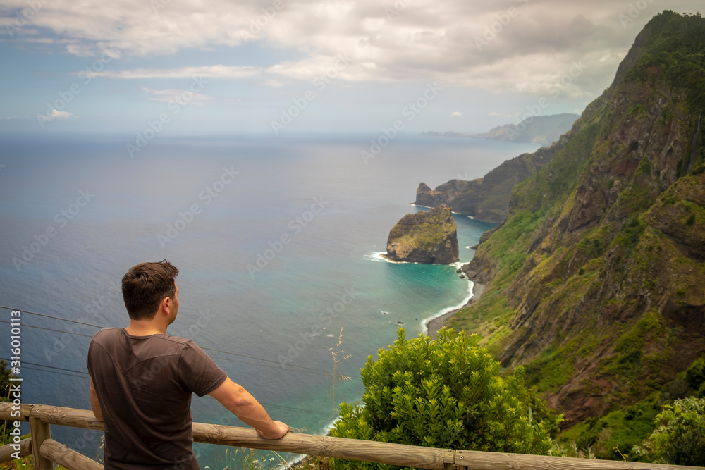 Homem a olhar para bonita paisagem de penhasco à beira mar e montanhas com vegetação