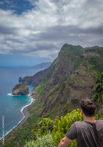 Homem a olhar para bonita paisagem de penhasco à beira mar e montanhas com vegetação © Romano Alves