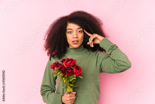 Young afro woman holding a roses isolated Young afro woman holding a rosespointing temple with finger, thinking, focused on a task.