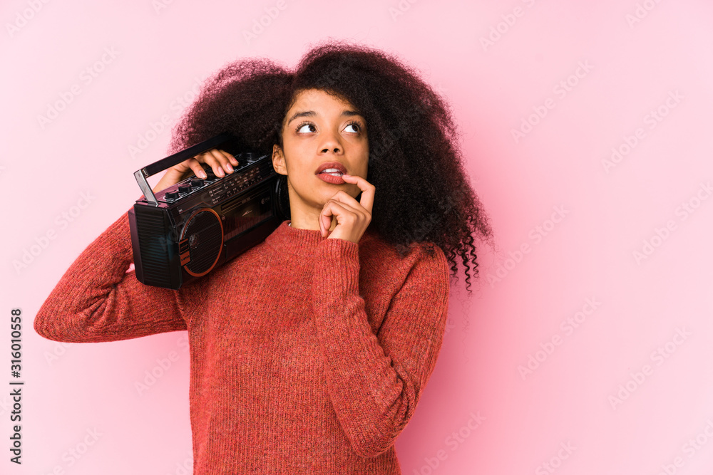 Young afro woman holding a cassete isolated relaxed thinking about something looking at a copy space. Young afro woman holding a cassete isolated relaxed thinking about something looking at a copy space.