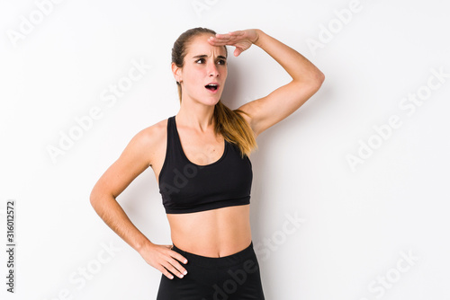 Young caucasian fitness woman posing in a white background looking far away keeping hand on forehead. © Asier