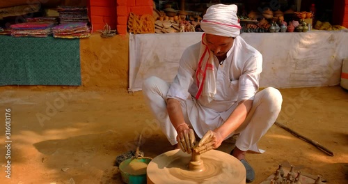 Skilled professional potter throwing the potter's wheel and shaping traditional ceramic vessel and clay ware: pot, jar in pottery workshop. Handwork craft from Shilpagram, Udaipur, Rajasthan, India photo