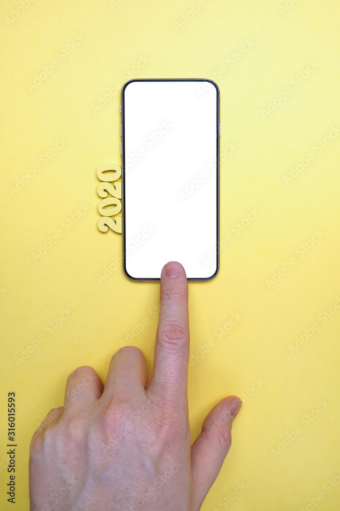 Abstract year 2020 of wooden letters next to a hand push to smartphone on a yellow background. Top view. Mock up. Copy space. Abstract year 2020 of wooden letters next to a hand push to smartphone on a yellow background. Top view. Mock up. Copy space.