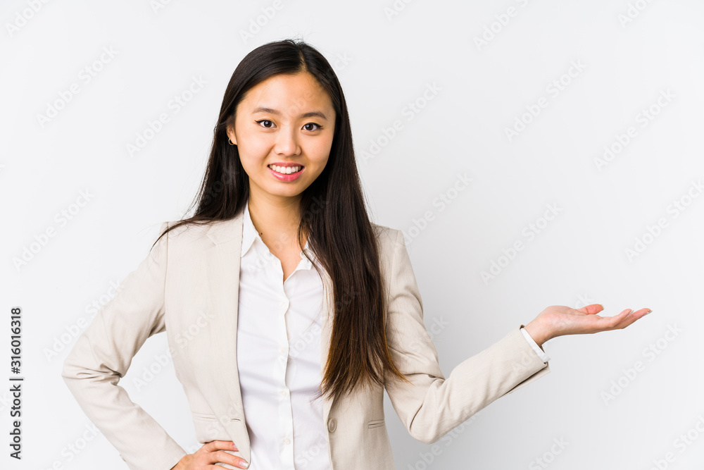 Young business chinese woman isolated showing a copy space on a palm and holding another hand on waist. Young business chinese woman isolated showing a copy space on a palm and holding another hand on waist.