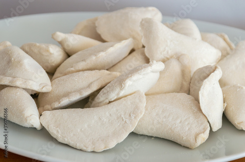 Raw frozen uncooked dumplings on white plate.