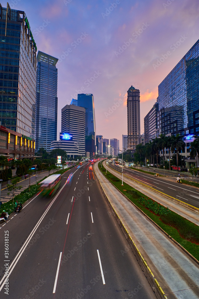Light trails on the busy traffic surrounded by Jakarta business office buildings with colorful sky