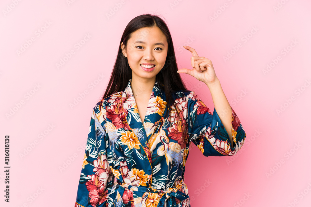 Young chinese woman wearing a kimono pajama isolated holding something little with forefingers, smiling and confident. Young chinese woman wearing a kimono pajama isolated holding something little with forefingers, smiling and confident.