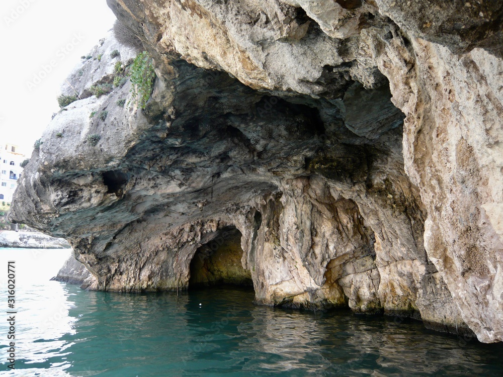 Turquoise water, shallow cave, and rock clinging shrubbery on overhanging cliff, nobody   