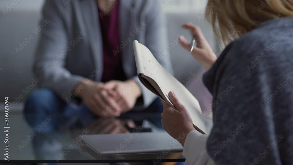 Rack focus view of female therapist asking questions to unrecognizable male patient, listening to answers and making notes in notepad