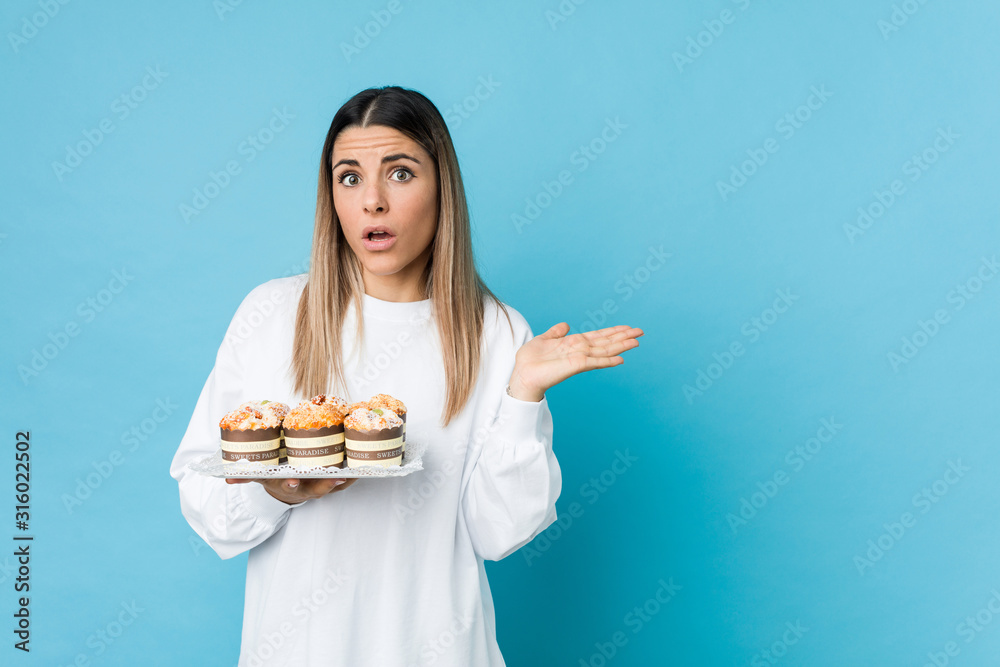 Young caucasian woman holding a sweets cake impressed holding copy space on palm. Young caucasian woman holding a sweets cake impressed holding copy space on palm.