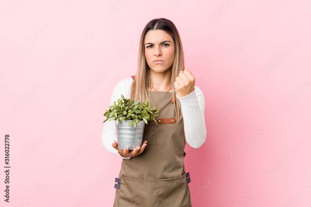 Young gardener woman holding a plant showing fist to camera, aggressive facial expression. Young gardener woman holding a plant showing fist to camera, aggressive facial expression.