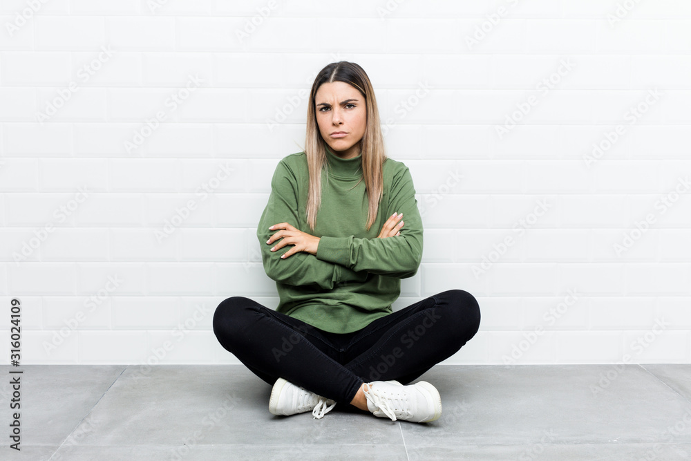 Young caucasian woman sitting on the floor frowning face in displeasure, keeps arms folded. Young caucasian woman sitting on the floor frowning face in displeasure, keeps arms folded.